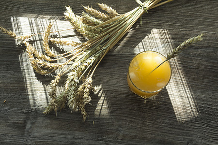 鲜榨的黄色果汁和成熟小麦的小穗在阳光下的木桌上。