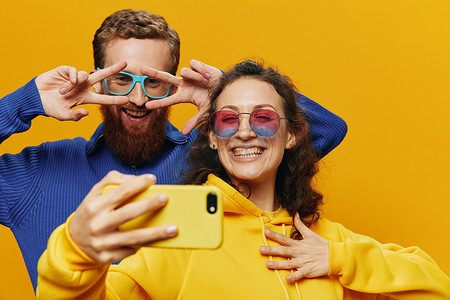 在黄色背景下，女人和男人带着手机的搞笑情侣手握社交网络和歪歪扭扭的交流自拍微笑很有趣。