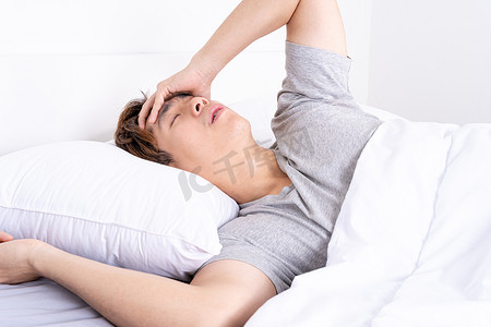 在床上醒来后患有头痛的年轻人。