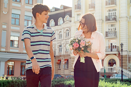 儿子十几岁和妈妈一起在户外散步，妈妈拿着花束
