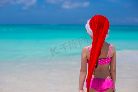 海滩上戴着红帽圣诞老人的可爱女孩的背影