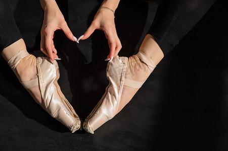 一位不露面的芭蕾舞演员坐在地板上，用她的手和足尖鞋做出一个心形。
