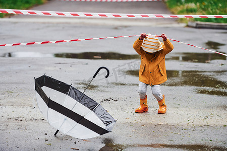防水雨伞摄影照片_雨后穿着黄色防水斗篷、靴子和雨伞在户外玩耍的孩子靠近保护带