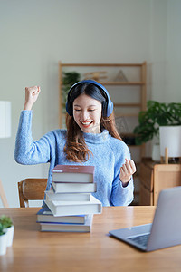 年轻美丽的亚洲女性在清晨在线课堂上以书籍、耳机和电脑作为家里的学习材料时露出笑脸的肖像