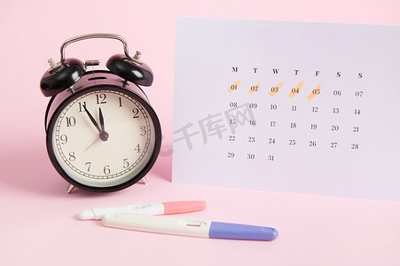 静物怀孕测试套件、闹钟和白色日历，上面标有上次月经的日期，粉红色背景