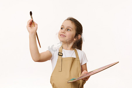 学龄前儿童白色背景中的肖像，可爱的小女孩拿着调色板，用画笔绘画