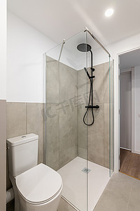 一间空荡荡的小浴室，里面有厕所和灰色瓷砖的玻璃淋浴间。