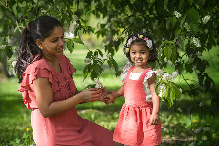 春天树叶鸟摄影照片_一个漂亮的黝黑女人在春天和她的女儿一起散步