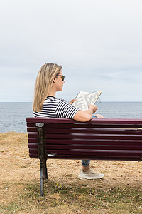 女人坐在海边的木凳上看书