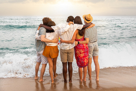 多种族朋友的后视图在假期旅行中拥抱在一起，看着大海放松。