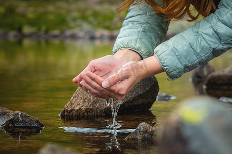 两手摄影照片_一个女人的手从她的手掌中倒水，同时试图从大自然中的清洁水源中喝水