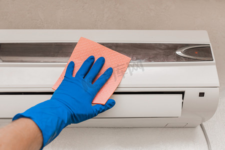 修整摄影照片_一个戴着蓝色橡胶家用手套的男人的手擦拭并清洁空调。