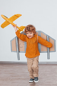 穿着复古飞行员制服的小男孩在室内带着玩具飞机跑