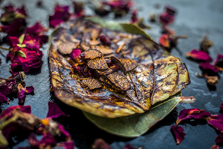 提水摄影照片_黑色表面上著名的印度传统马萨拉锅或 meetha 锅的特写，上面有一些玫瑰水，包括涂有 sauf、supari、甜味剂和一些椰子粉。