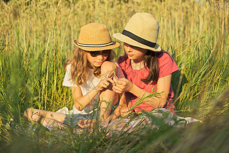 两个微笑的女孩坐在草地上，孩子们在说话