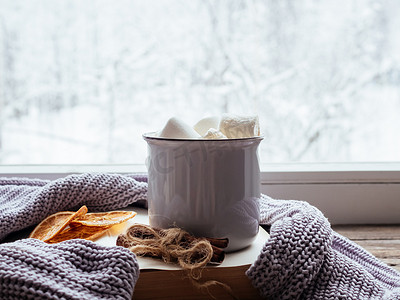 复古窗台上的咖啡配棉花糖、肉桂、书籍和舒适的灰色毛衣，与外面的雪景相映成趣。