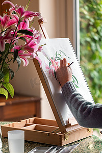 年轻的左撇子女孩在家里的画架上画着鲜花、紫色百合和水彩画的静物画
