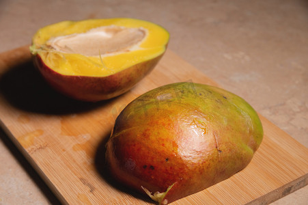 芒果加工摄影照片_芒果，鲜熟芒果的特写，切成两半，放在切木板上