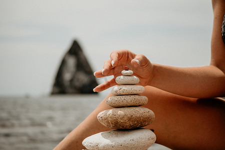在阳光明媚的日子里，女人在海边建造一座石头金字塔。