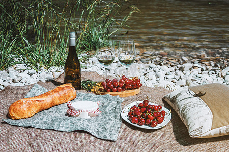 地毯花纹摄影照片_浪漫的乡村野餐，带两个白酒杯、瓶子、法式面包、奶酪、开放书