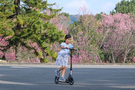夏日，可爱的小女孩在室外公园的街道上骑滑板车。