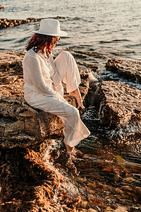 男式裤装摄影照片_一位穿着白色裤装和帽子的女人站在沙滩上享受大海。
