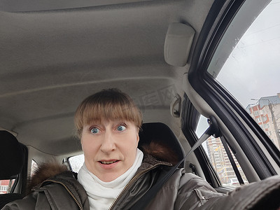 成年可爱有趣的金发女人穿着暖和的衣服在车里自拍并驾驶它的画像。