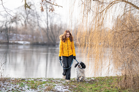 散步摄影照片_的女孩和她的狗在大自然的湖边散步。