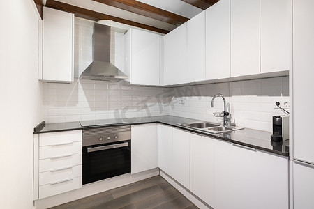 白色大理石台面摄影照片_经典风格的现代轻型厨房，配有白色木质角柜、光滑的深色大理石台面和白色墙砖。