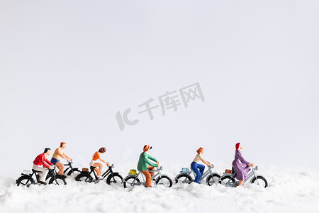 微型人物：在雪地背景上骑自行车的旅行者