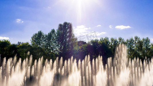 在夏季喷泉中飞溅和滴落。喷泉背景下的日落，美丽的蓝天，流动的水在风中飞溅。