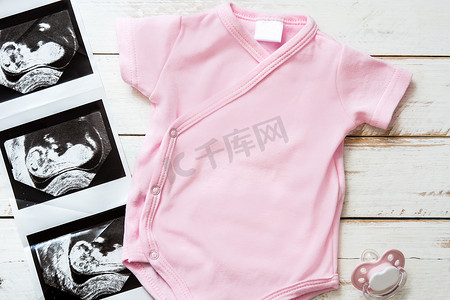白色木制背景上的粉红色婴儿连身衣和超声波婴儿。