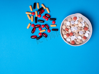 一碗药丸的顶视图，旁边是不同颜色和形状的其他药丸和胶囊