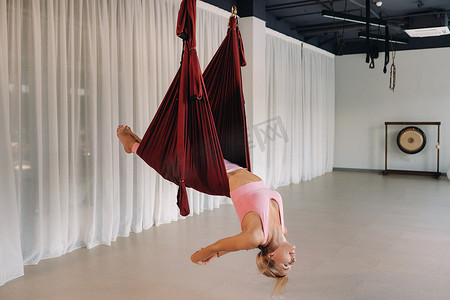 一位身为空中瑜伽教练的少女，正吊在瑜伽会馆大厅的吊床上。