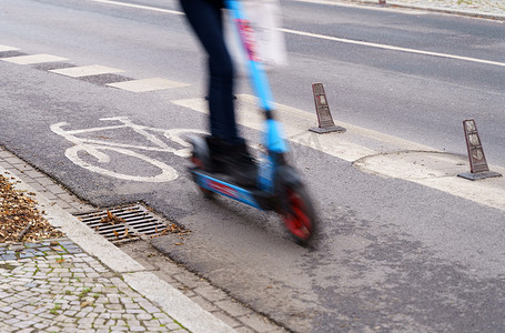 电动车道摄影照片_一位女士骑着电动滑板车沿着自行车道行驶。