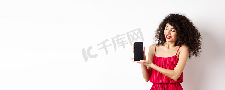 化妆和卷发的美女，展示空的智能手机屏幕，展示应用程序，站在白色背景上