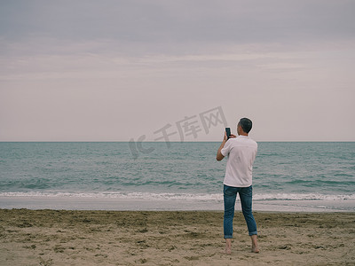 一个人在海边用智能手机相机拍照