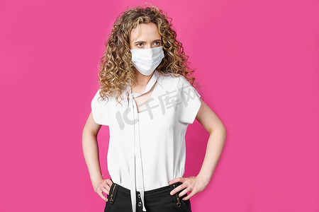 一名脸上戴着医用口罩的年轻女子双手叉腰站立。
