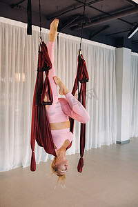一位身为空中瑜伽教练的少女，正吊在瑜伽会馆大厅的吊床上。