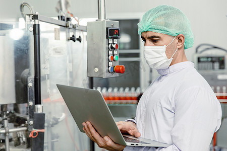 工程师在食品厂机器生产检查员和卫生服中使用笔记本电脑。