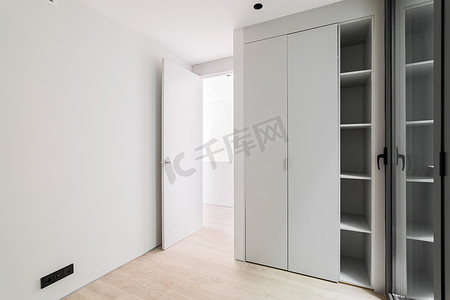 滑动衣柜摄影照片_现代风格的内饰、中性白色走廊、木质浅色镶木地板、滑动衣柜和黑色铝框玻璃门