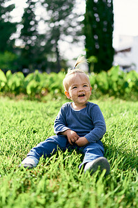 树木的孩子摄影照片_有马尾辫的笑的孩子坐在绿色草坪上