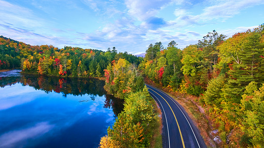 俯瞰池塘摄影照片_空中俯瞰蓝湖旁的道路，四周环绕着秋季森林