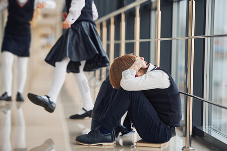 孩子难过摄影照片_穿着制服的男孩独自坐在学校里感到难过。