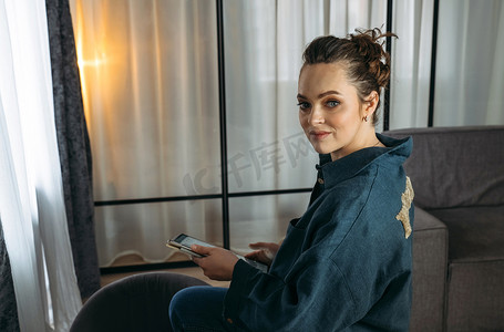 窗户台摄影照片_一位穿着深蓝色西装的年轻女子坐在沙发靠背上，手里拿着一台平板电脑。