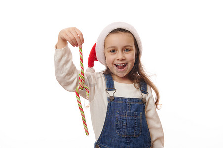 戴着圣诞帽、笑得开朗的小女孩，在白色背景上玩着条纹红绿棒棒糖