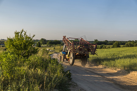 一辆带农用拖车的蓝色拖拉机沿着麦田的道路行驶。