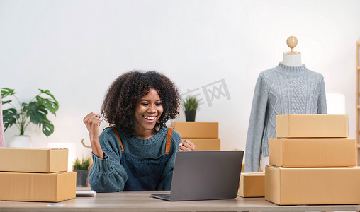 快乐的年轻亚洲女企业家，在家庭办公室用智能手机查看在线购物商店的订单后，为销售成功而微笑，在线商业和电子商务的概念
