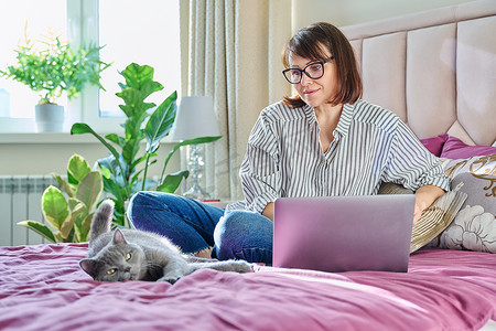 家里的中年妇女躺在床上，带着笔记本电脑和猫