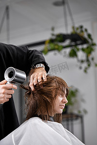 男人吹头发摄影照片_男士美发师洗完后用吹风机吹干女性头发